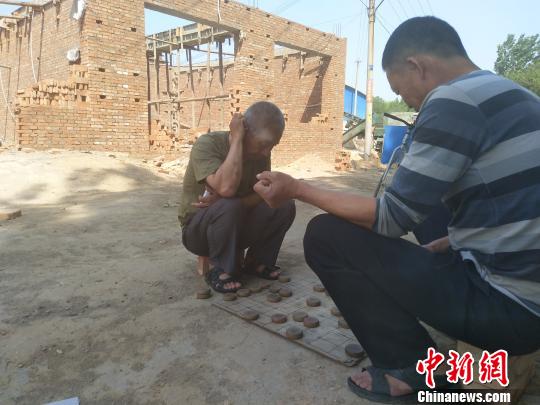 雄安新区小王营村一栋停建的平房前，两位村民正在下棋。　王天译　摄
